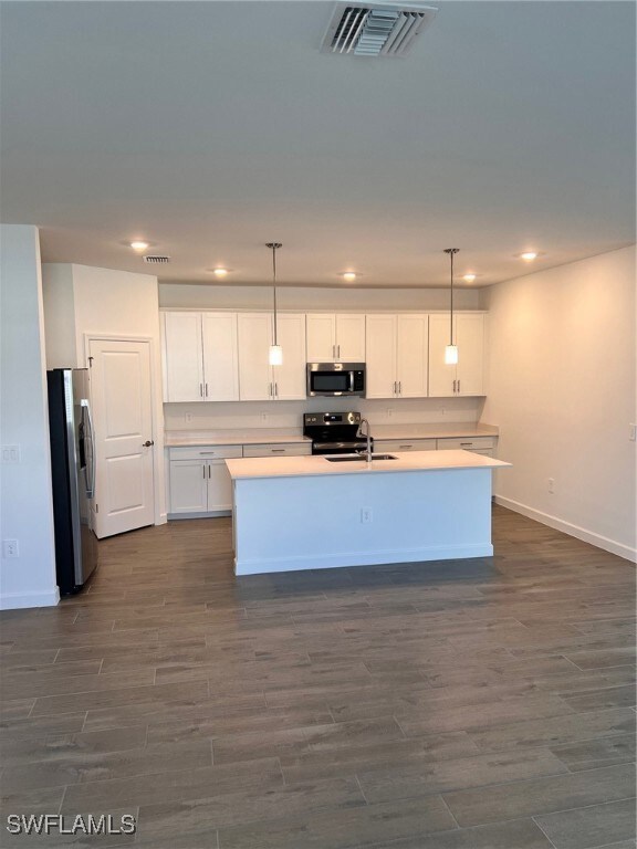 Kitchen featuring dark hardwood / wood-style flooring, appliances with stainless steel finishes, white cabinets, and a kitchen island with sink