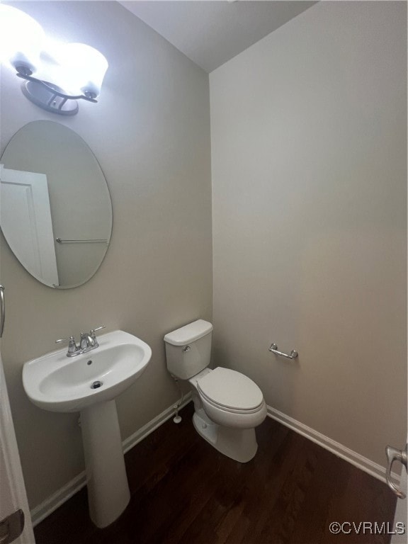 Half bathroom featuring wood finished floors, toilet, and baseboards