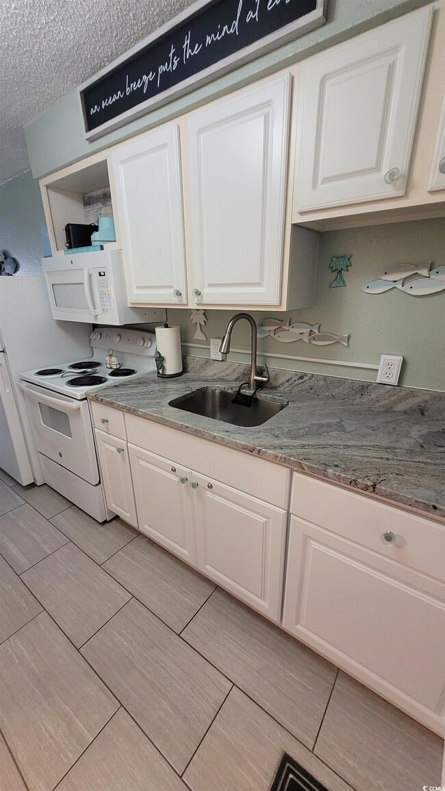 Kitchen with white appliances, white cabinets, open shelves, light stone counters, and a textured ceiling