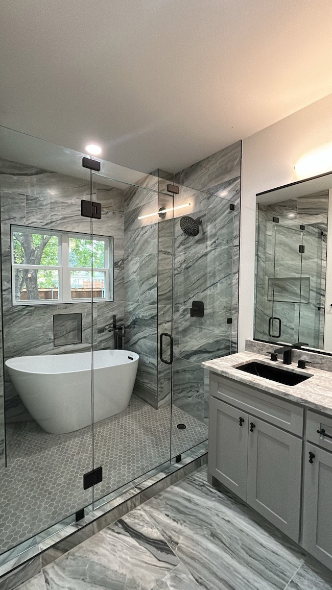 Bathroom with vanity, tile walls, light marble finish floors, a marble finish shower, and a soaking tub