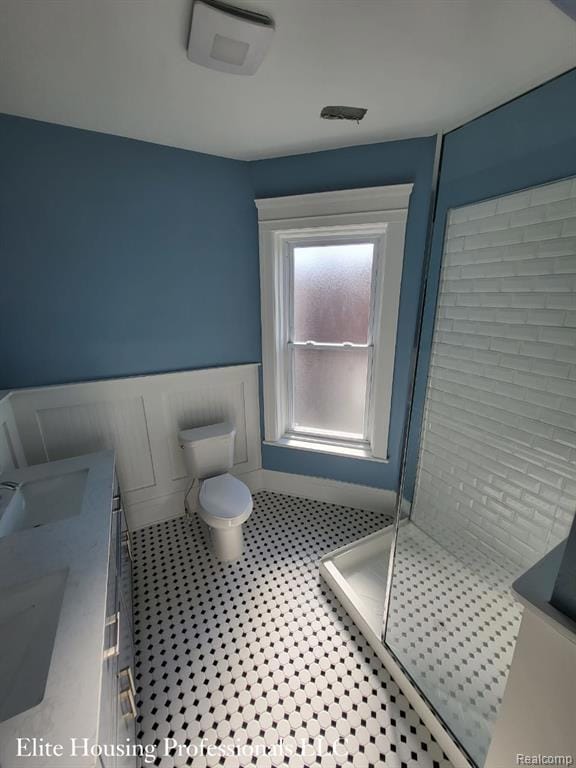 Full bath featuring double vanity, a shower stall, and wainscoting