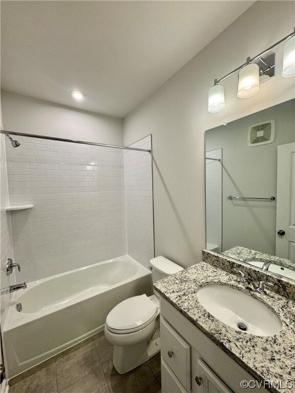 Full bathroom with tile flooring, tiled shower / bath, large vanity, and toilet