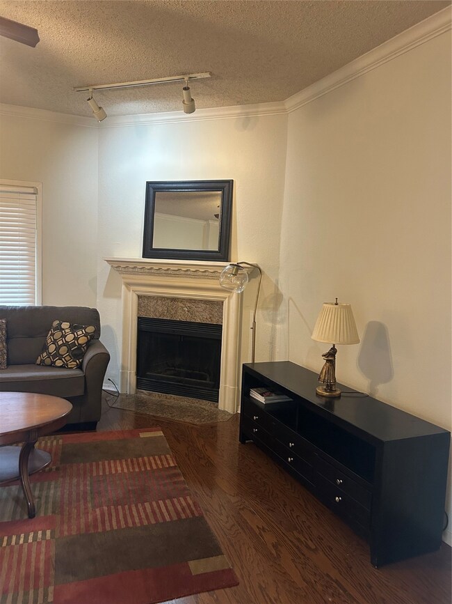 Living room featuring track lighting, dark wood finished floors, a premium fireplace, ornamental molding, and a textured ceiling