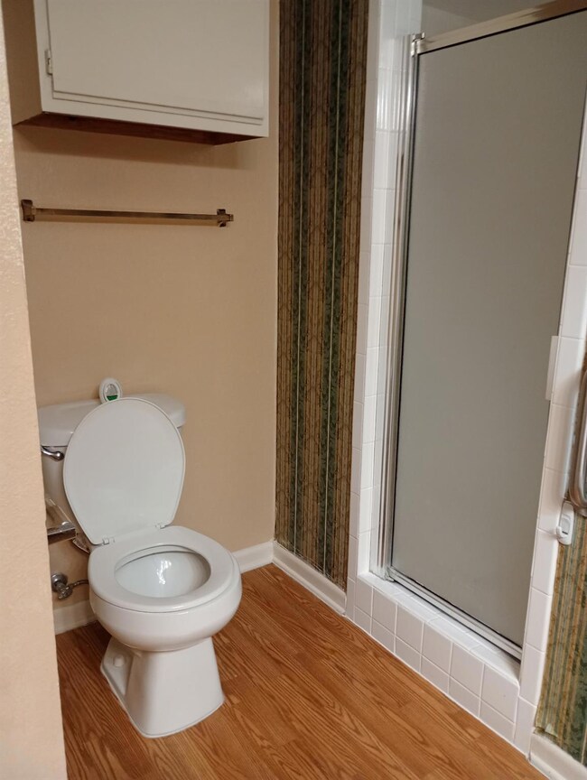 Full bath featuring a stall shower, toilet, wood 