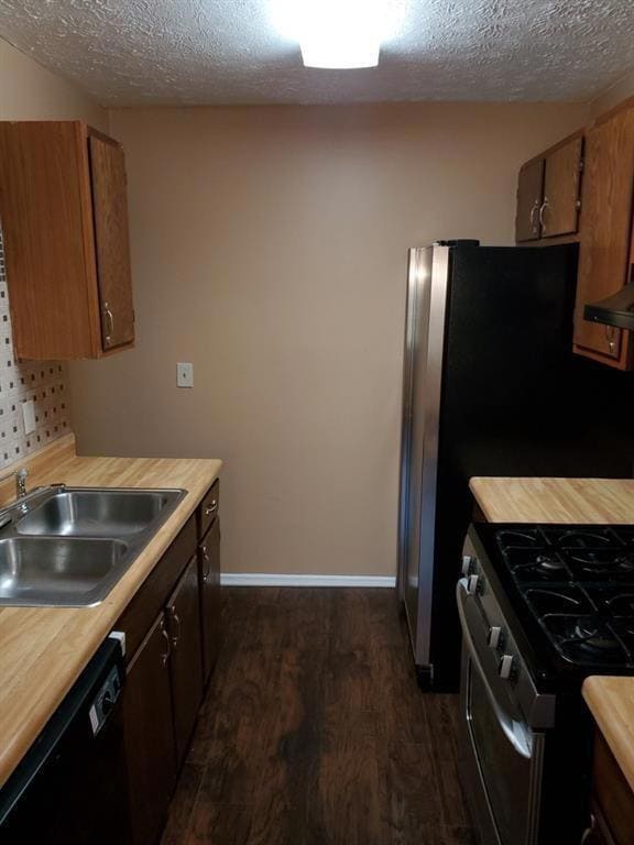 Kitchen featuring black dishwasher, stainless steel range with gas stovetop, dark wood-style flooring, a textured ceiling, and brown cabinetry