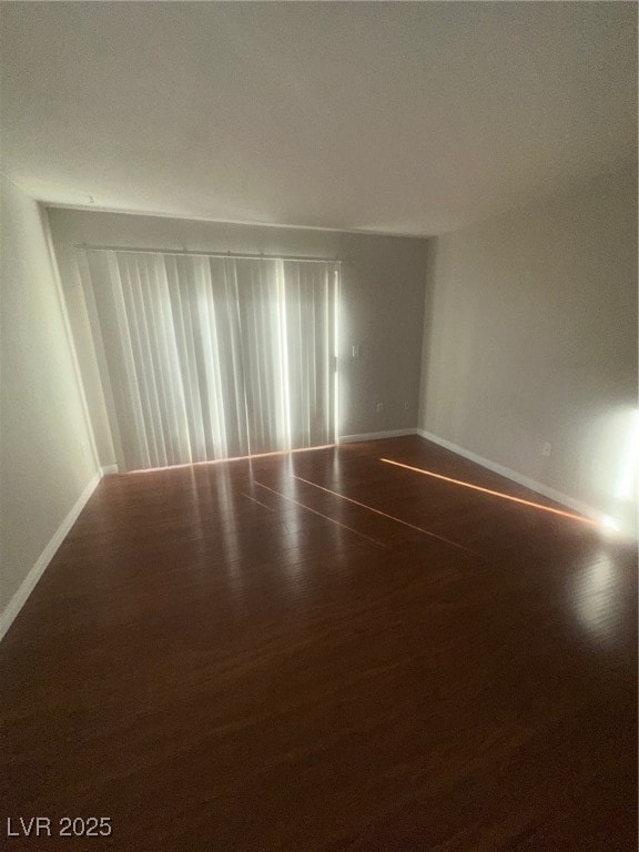 Spare room featuring dark wood-style floors and baseboards