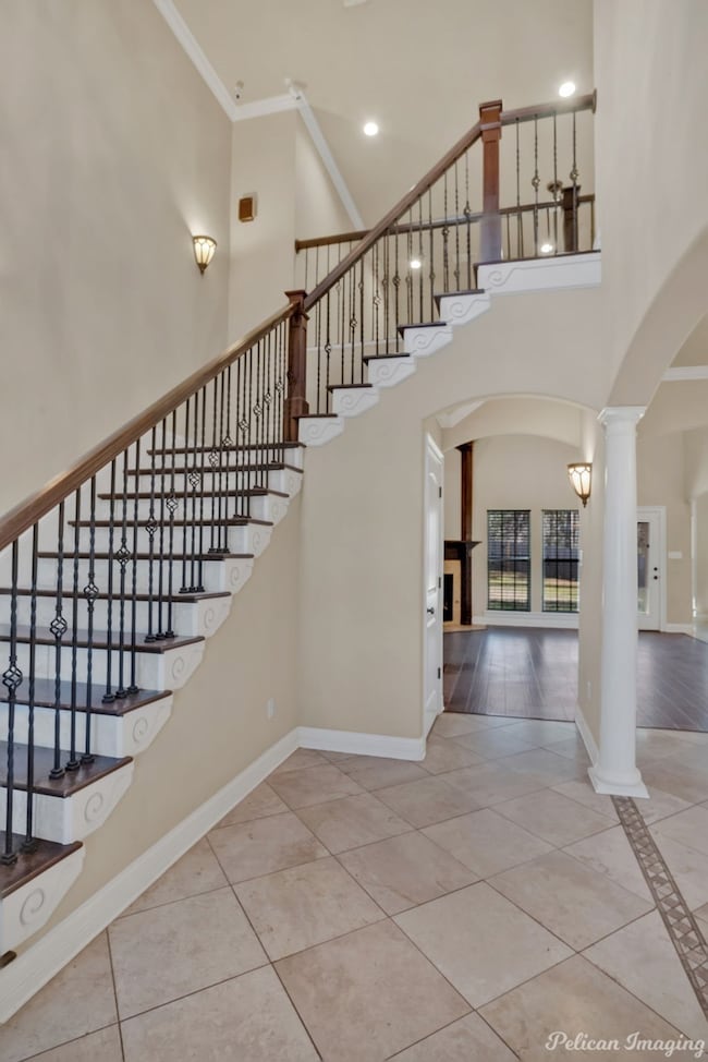 Stairway featuring arched walkways, ornate columns, a towering ceiling, tile patterned flooring, and crown molding