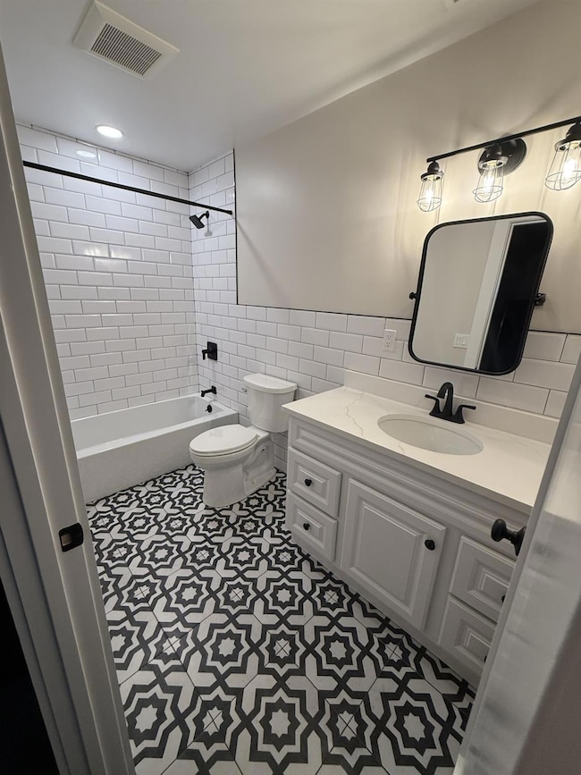 Bathroom with toilet, vanity, tile walls, bathtub / shower combination, and tile patterned floors