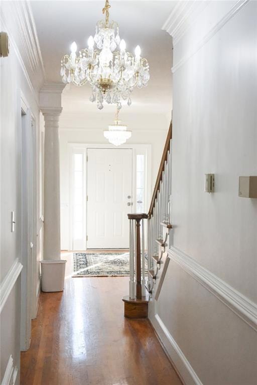 Entrance foyer with wood finished floors, crown molding, stairs, a chandelier, and decorative columns