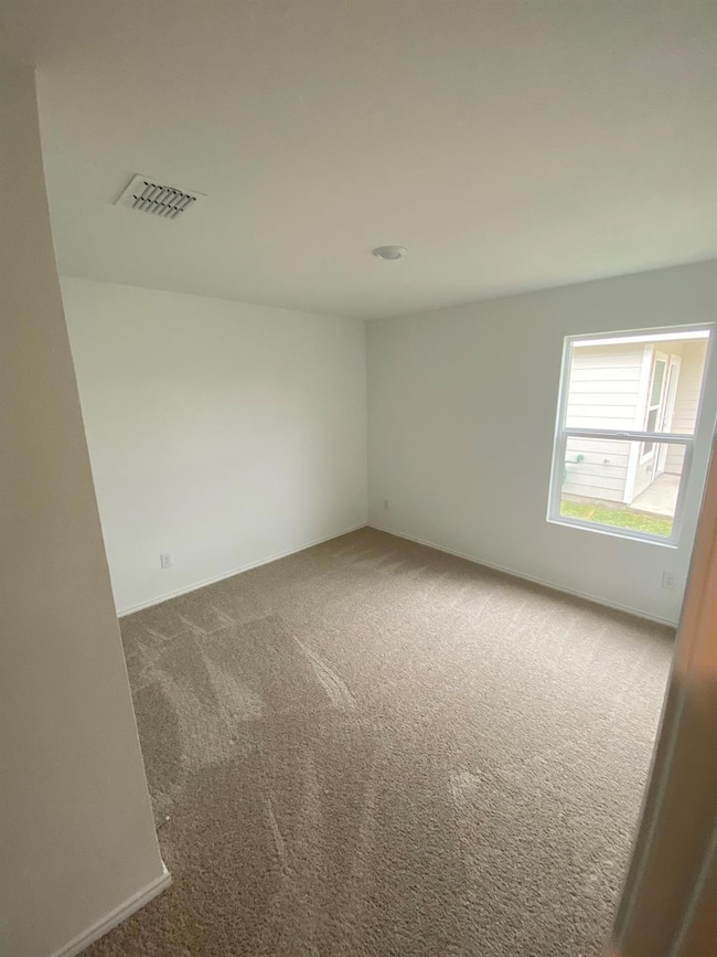 Carpeted empty room with visible vents and baseboa