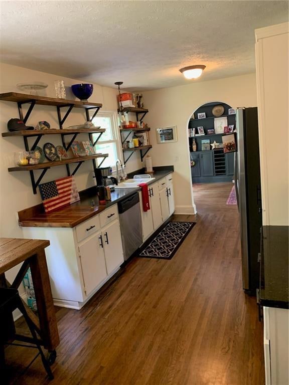 Kitchen featuring open shelves, dishwashing machine, dark countertops, arched walkways, and a textured ceiling
