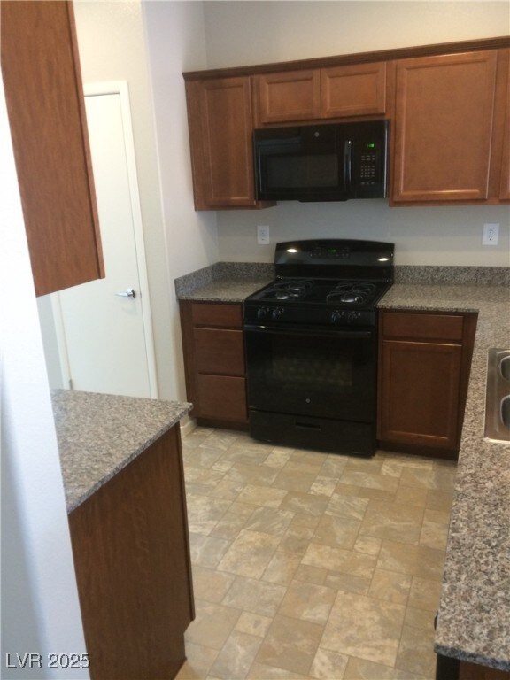 Kitchen featuring black appliances, brown cabinetry, and stone finish floors