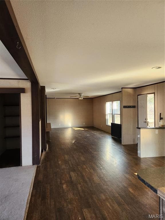 Unfurnished living room with a textured ceiling, ceiling fan, and dark wood-type flooring