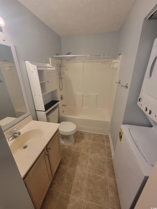 Bathroom featuring stacked washing machine and dryer, vanity, toilet, bathtub / shower combination, and a textured ceiling