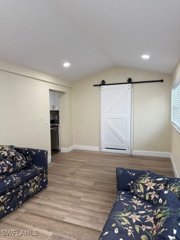 Living area featuring a barn door, light wood-style flooring, vaulted ceiling, and recessed lighting
