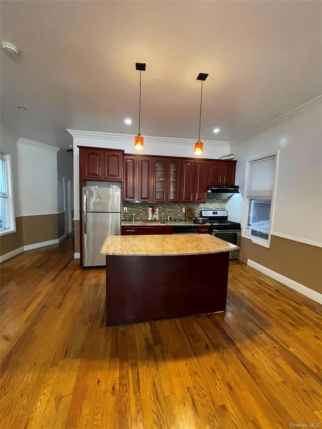 Kitchen with ornamental molding, hanging light fixtures, appliances with stainless steel finishes, a center island, and tasteful backsplash