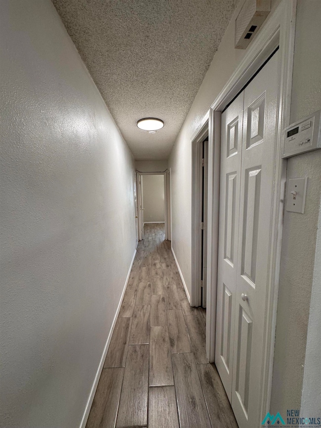 Corridor featuring a textured ceiling, light wood-style floors, and a textured wall