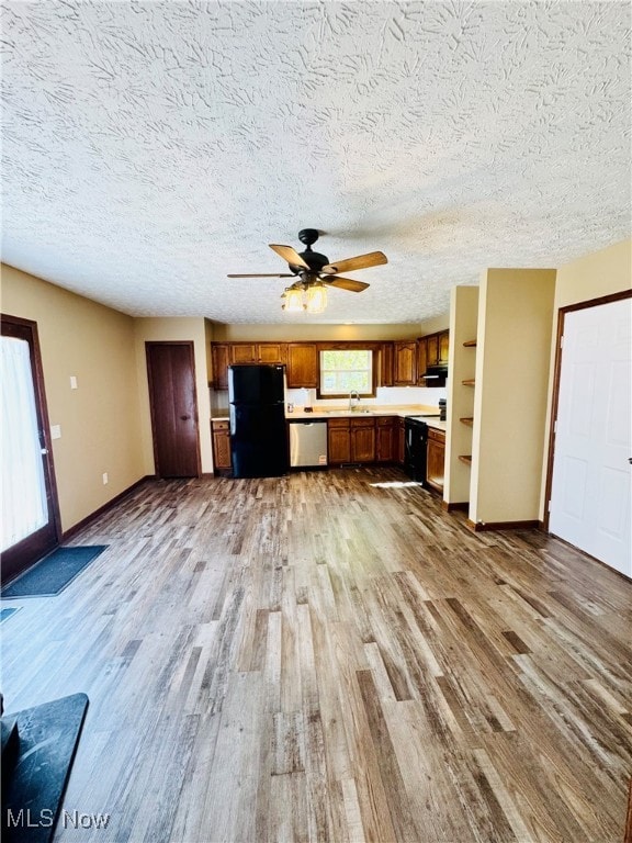 Kitchen with light wood-type flooring, brown cabinets, a textured ceiling, light countertops, and black appliances