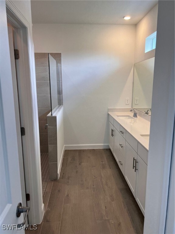 Bathroom with hardwood / wood-style floors, a tile shower, and vanity
