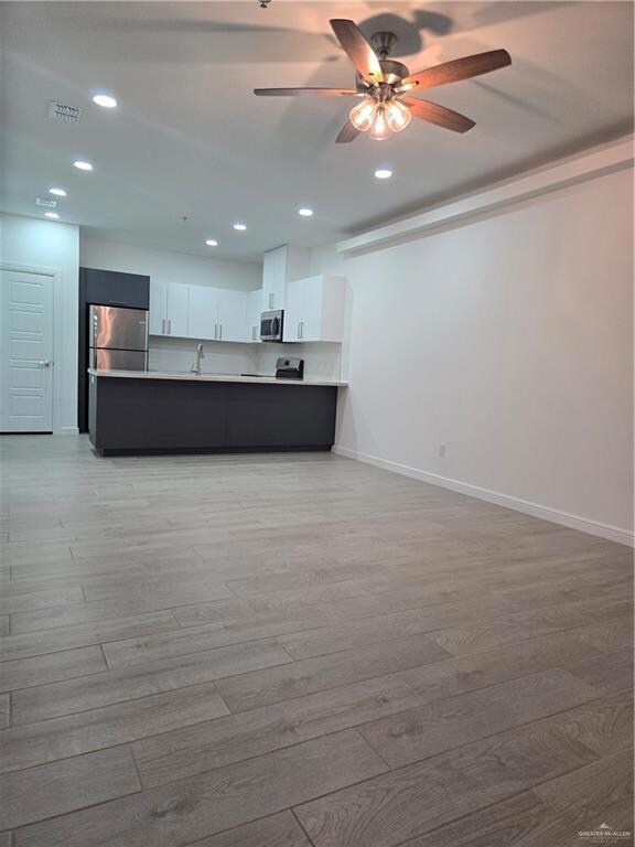 Kitchen featuring white range, kitchen peninsula, refrigerator, white cabinets, and light wood-type flooring