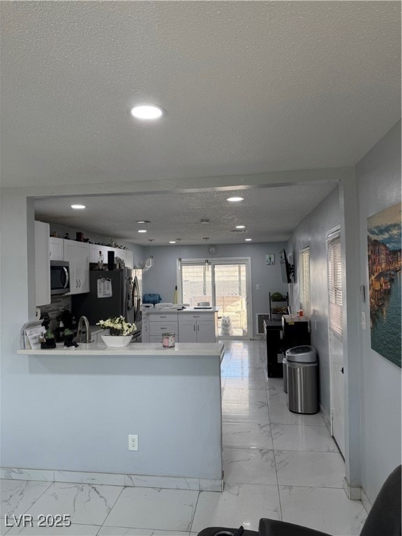 Kitchen with light marble finish floors, a textured ceiling, a peninsula, light countertops, and white cabinetry