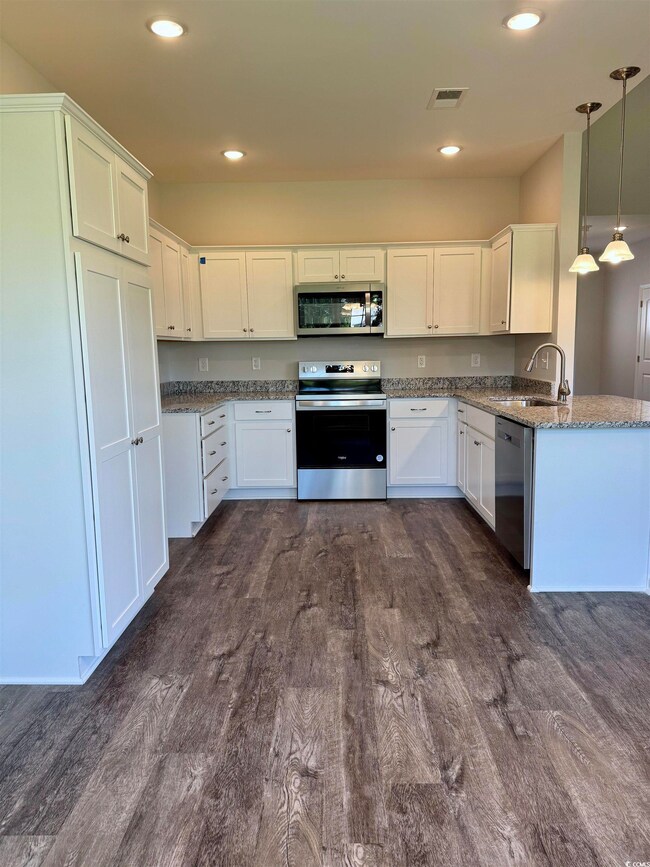 Kitchen featuring appliances with stainless steel finishes, white cabinets, dark wood-type flooring, hanging light fixtures, and dark stone countertops