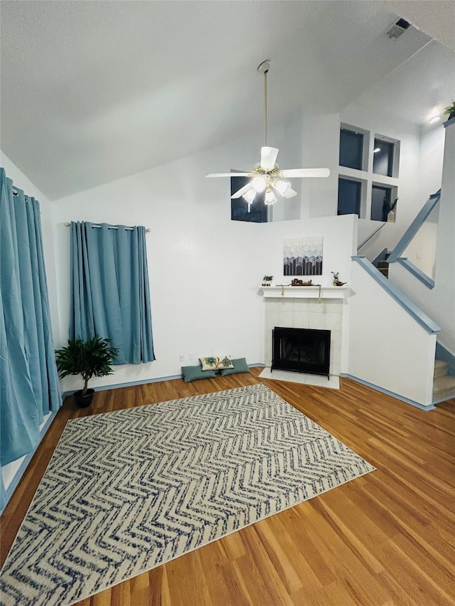 Living area featuring a tiled fireplace, wood finished floors, vaulted ceiling, stairs, and a ceiling fan