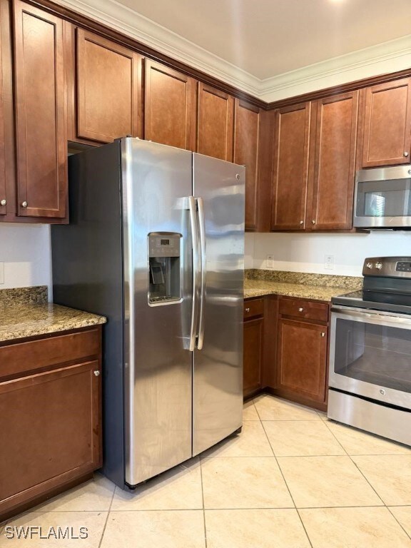 Kitchen featuring stone counters, light tile patterned flooring, ornamental molding, and appliances with stainless steel finishes