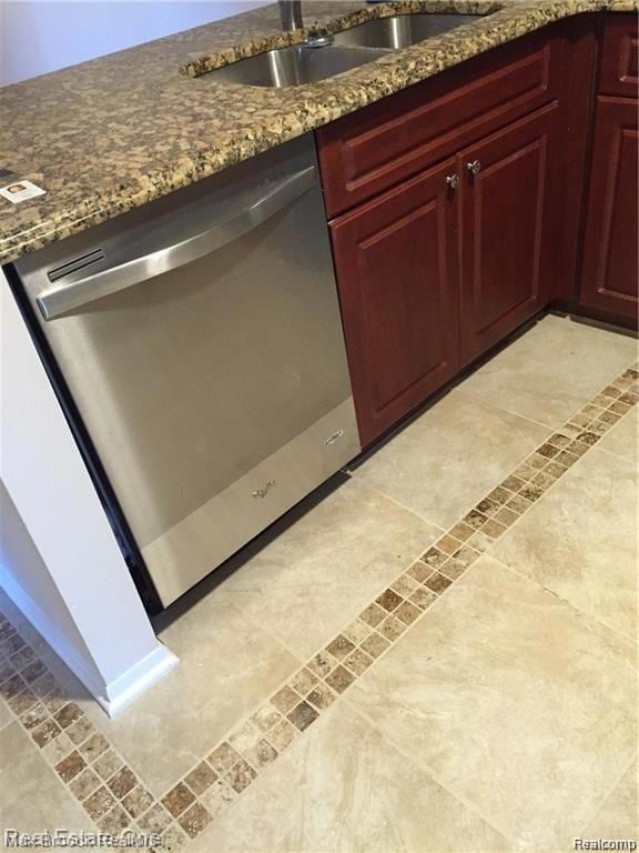 Kitchen view of stainless steel dishwasher, inlaid floor details, reddish brown cabinets, and stone counters