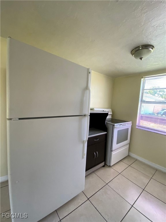 Kitchen with white appliances, light tile patterned floors, and a textured ceiling