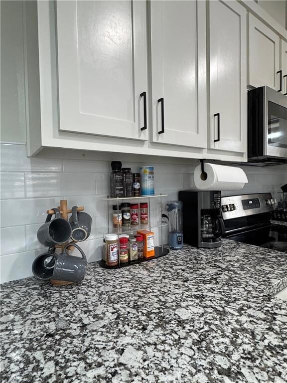 Kitchen featuring tasteful backsplash, white cabinetry, stainless steel microwave, and dark stone counters