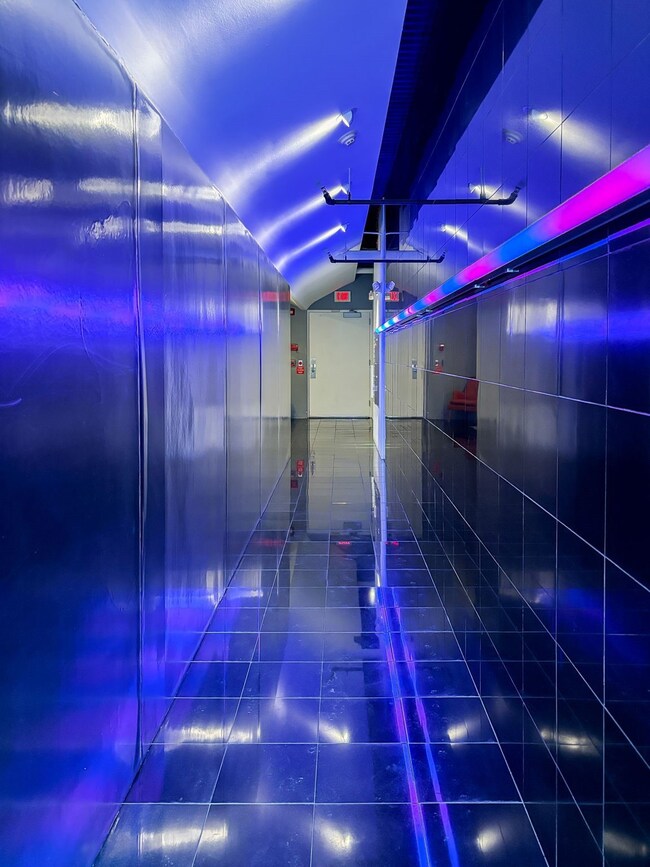 Enter building through neon lit hallway. lights co