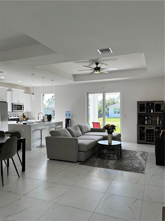 Living room with a tray ceiling, a ceiling fan, visible vents, recessed lighting, and marble finish floor
