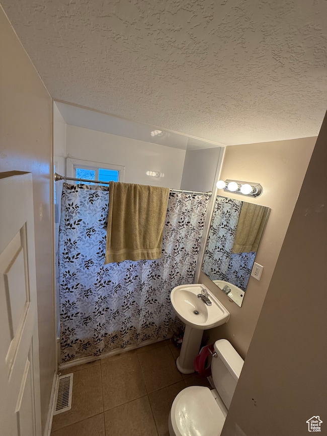 Full bathroom featuring tile patterned flooring, toilet, a textured ceiling, a shower with shower curtain, and a sink