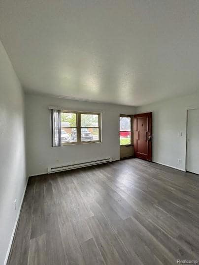 Unfurnished living room featuring dark wood-style floors and a baseboard radiator