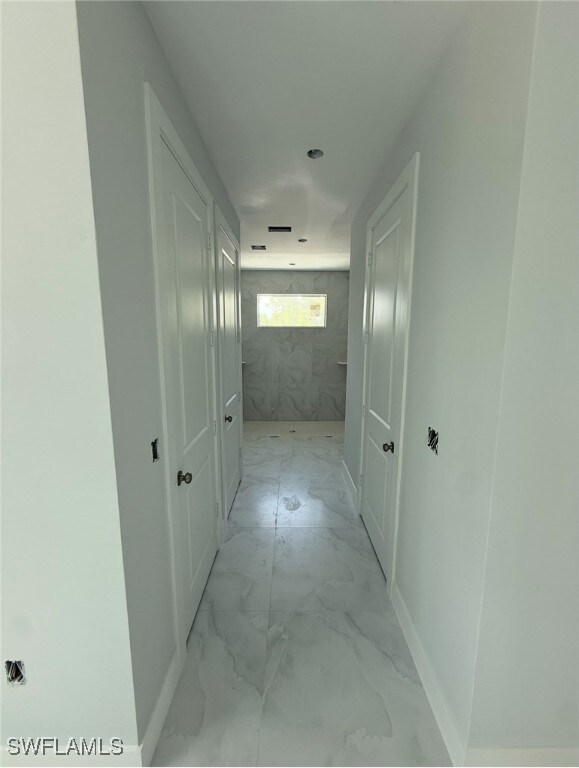 Hallway with light marble finish floors and basebo