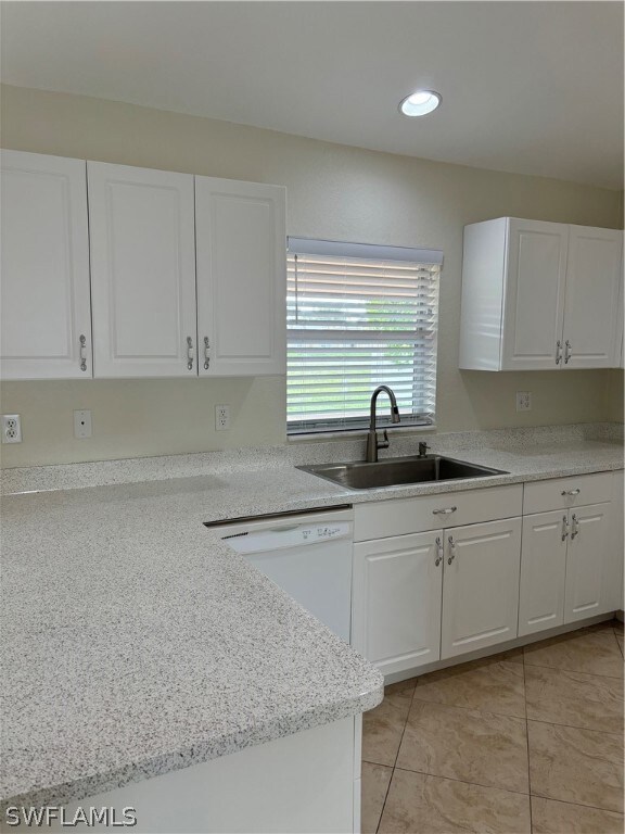 Kitchen featuring sink, dishwashing machine, white cabinets, and light tile flooring