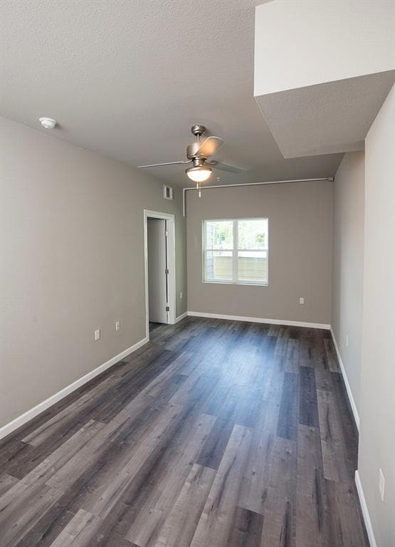 Empty room featuring dark wood-type flooring and a ceiling fan