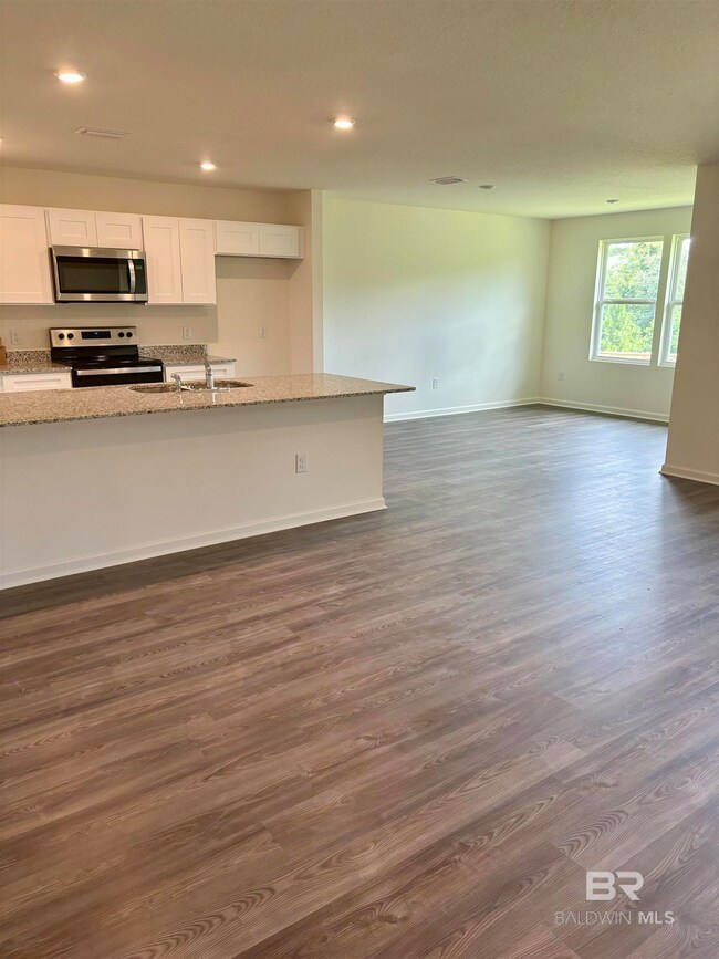 Kitchen featuring light stone counters, stainless steel appliances, white cabinetry, sink, and dark wood-type flooring