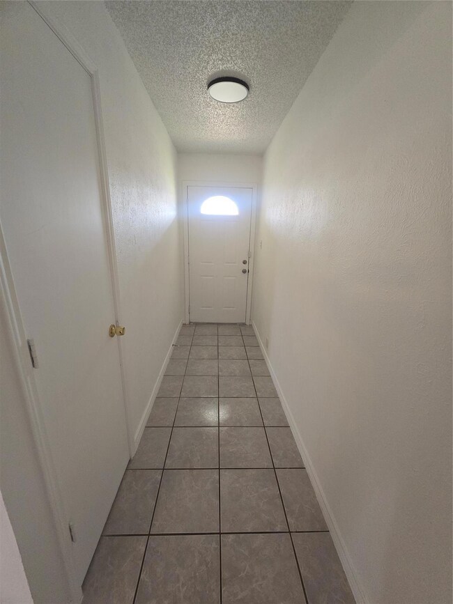 Corridor with light tile patterned flooring and a textured ceiling