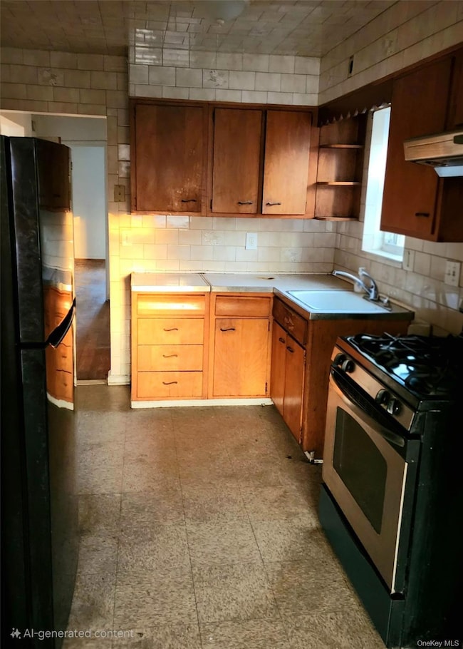 Kitchen with stainless steel gas stove, light countertops, under cabinet range hood, freestanding refrigerator, and open shelves