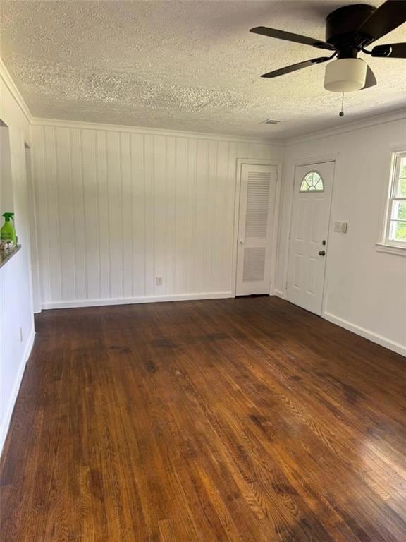 Unfurnished living room with ornamental molding, a textured ceiling, dark wood-type flooring, and ceiling fan