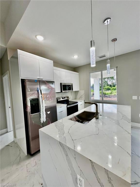 Kitchen with appliances with stainless steel finishes, pendant lighting, sink, white cabinets, and light stone counters