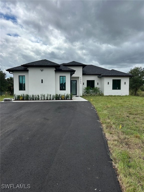 Prairie-style house with stucco siding, a front lawn, and roof with shingles