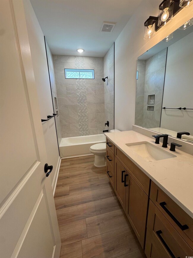 Full bath featuring vanity, toilet, visible vents,  shower combination, and wood finished floors
