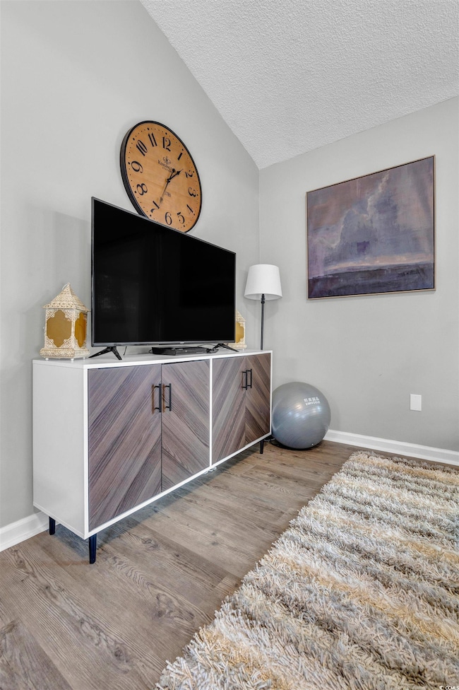 Bedroom featuring a textured ceiling, wood finished floors, and lofted ceiling