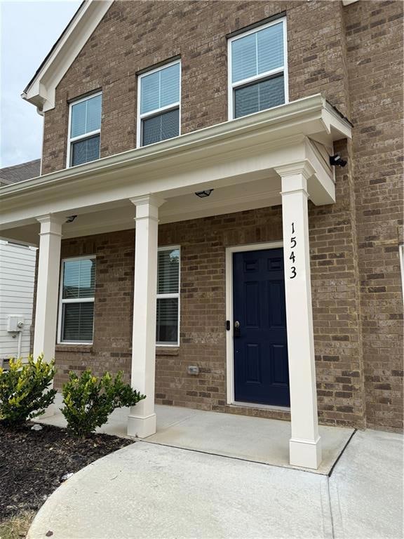 Entrance to property featuring brick siding and covered porch