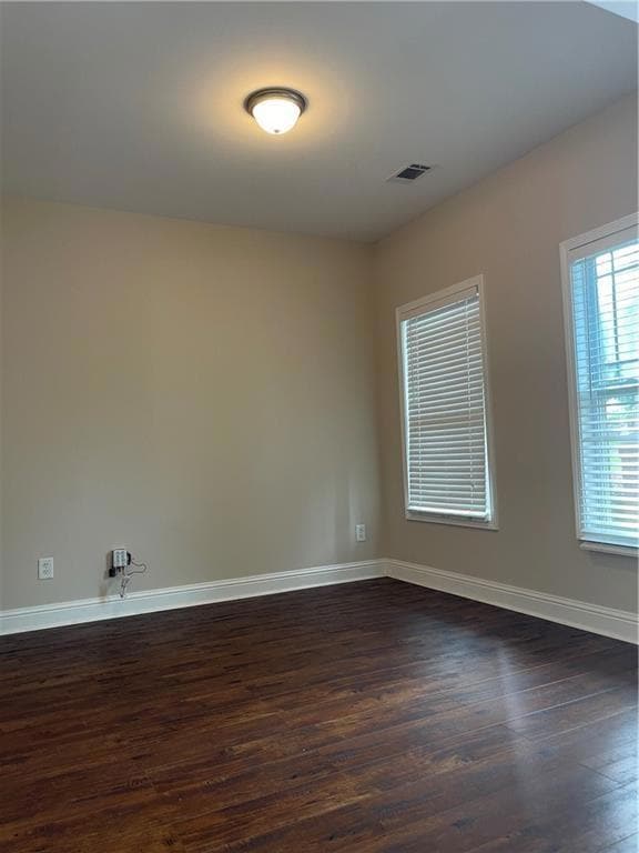 Spare room featuring dark wood-style floors and baseboards