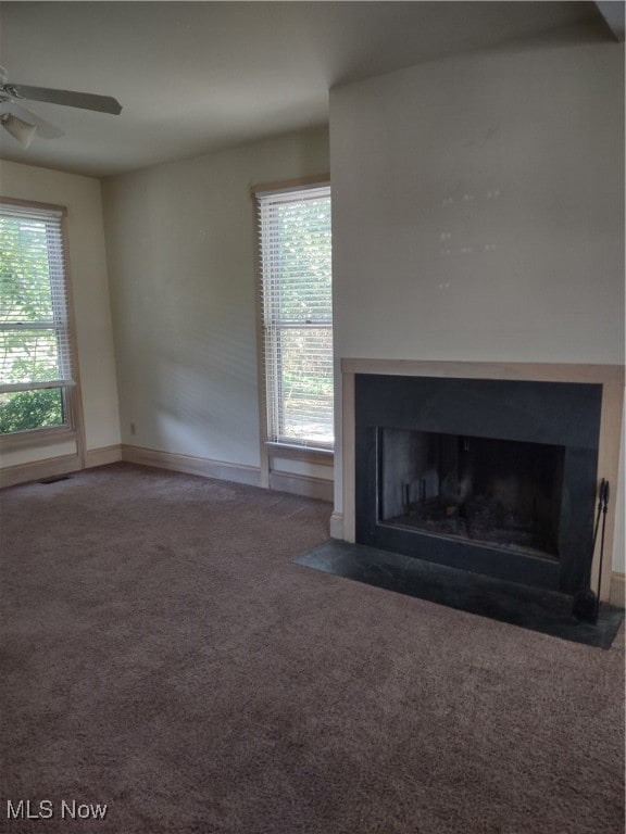 Unfurnished living room with healthy amount of natural light, carpet flooring, a fireplace with flush hearth, and a ceiling fan