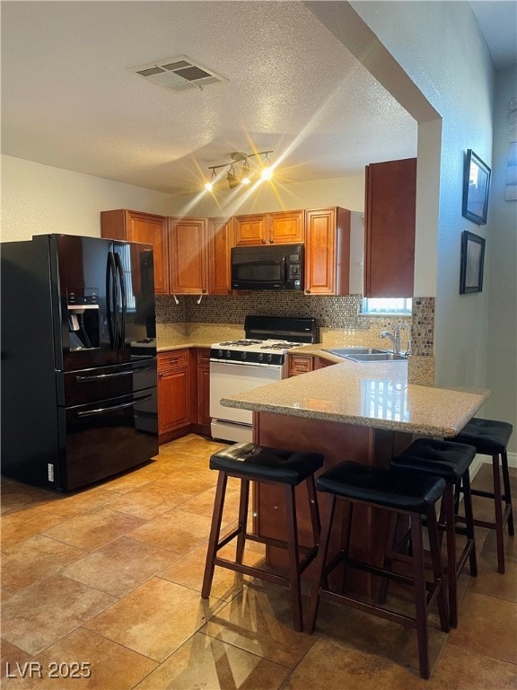 Kitchen featuring black appliances, backsplash, a peninsula, a breakfast bar area, and a textured ceiling